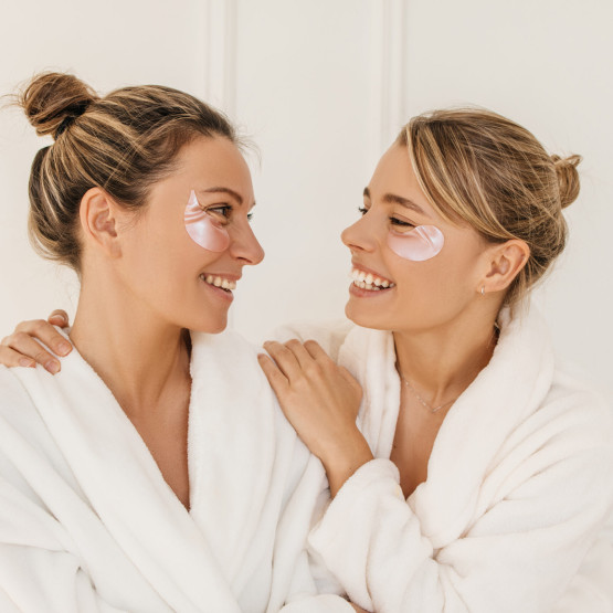 Attractive caucasian young girls in bathrobes are smiling looking at each other on white background.